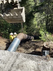 Construction crews installing a corrugated steel culvert beneath a California highway embankment.