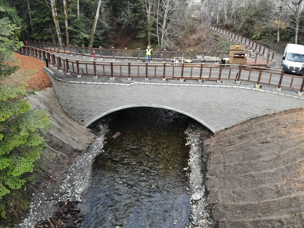 Aerial view of the completed Padden Creek crossing showing the Interurban Trail, steel arch, and restored stream corridor.