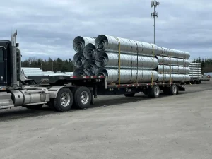 Corrugated steel pipe sections stacked and nested on a flatbed truck to maximize shipping capacity.
